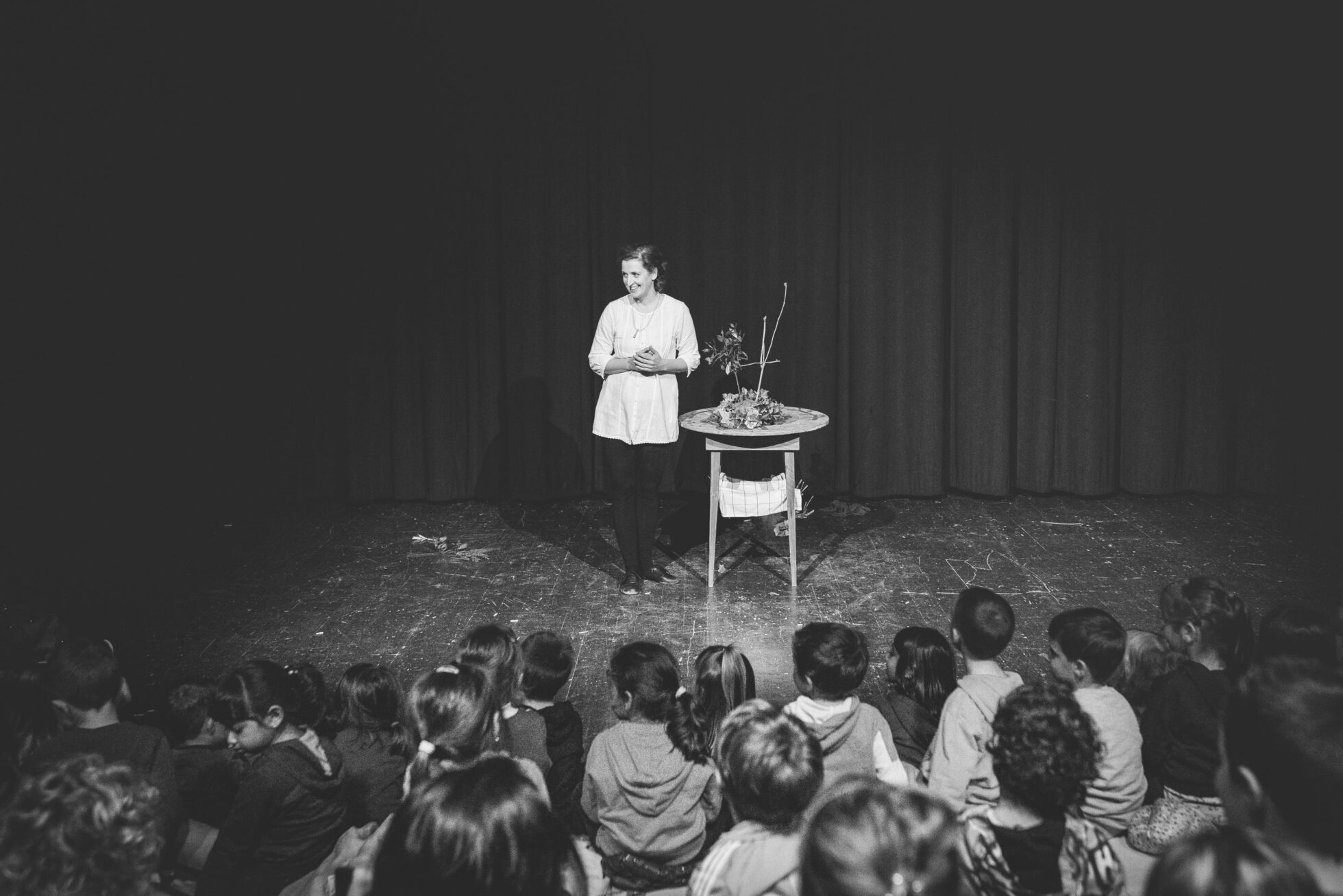 foto in bianco e nero di un'attrice in scena con i bambini seduti di fronte a lei sul palco