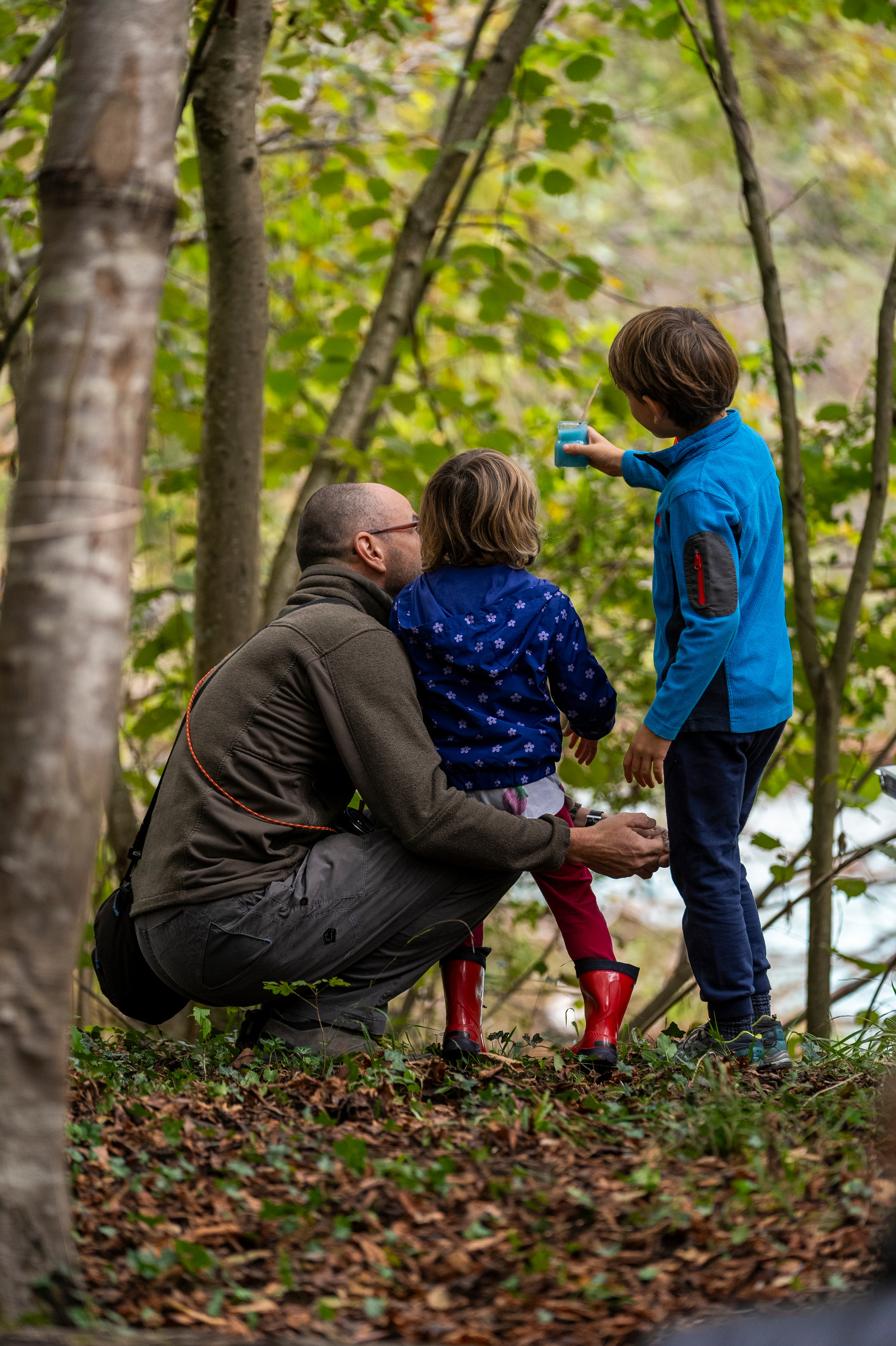 Un adulto assieme a due bambini nel bosco osservano un vaso con acqua colorata