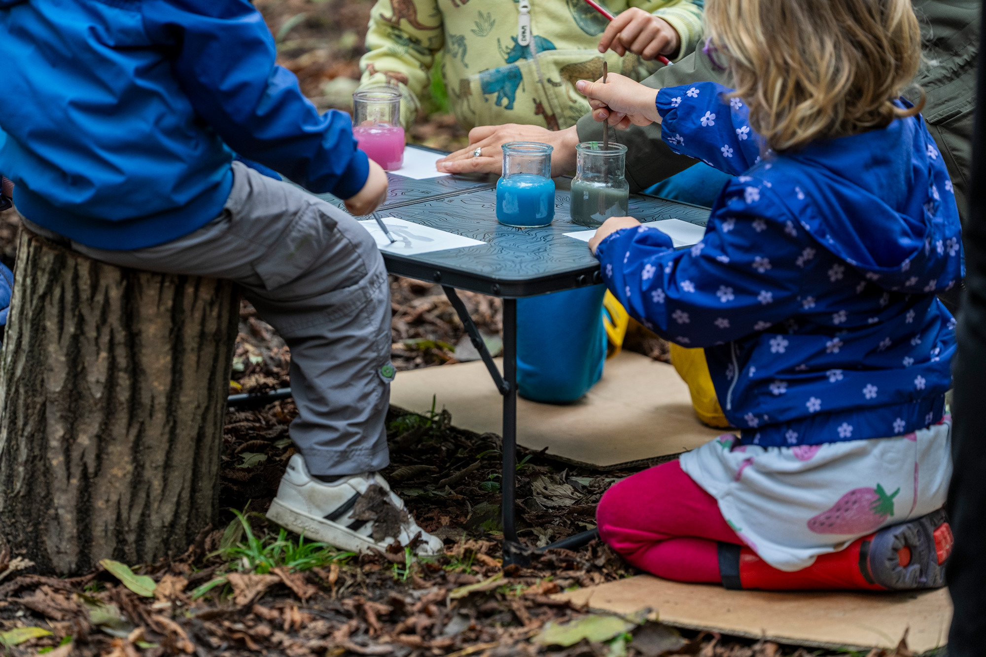 bambini seduti a terra che creano acque colorate durante un laboratorio nel bosco