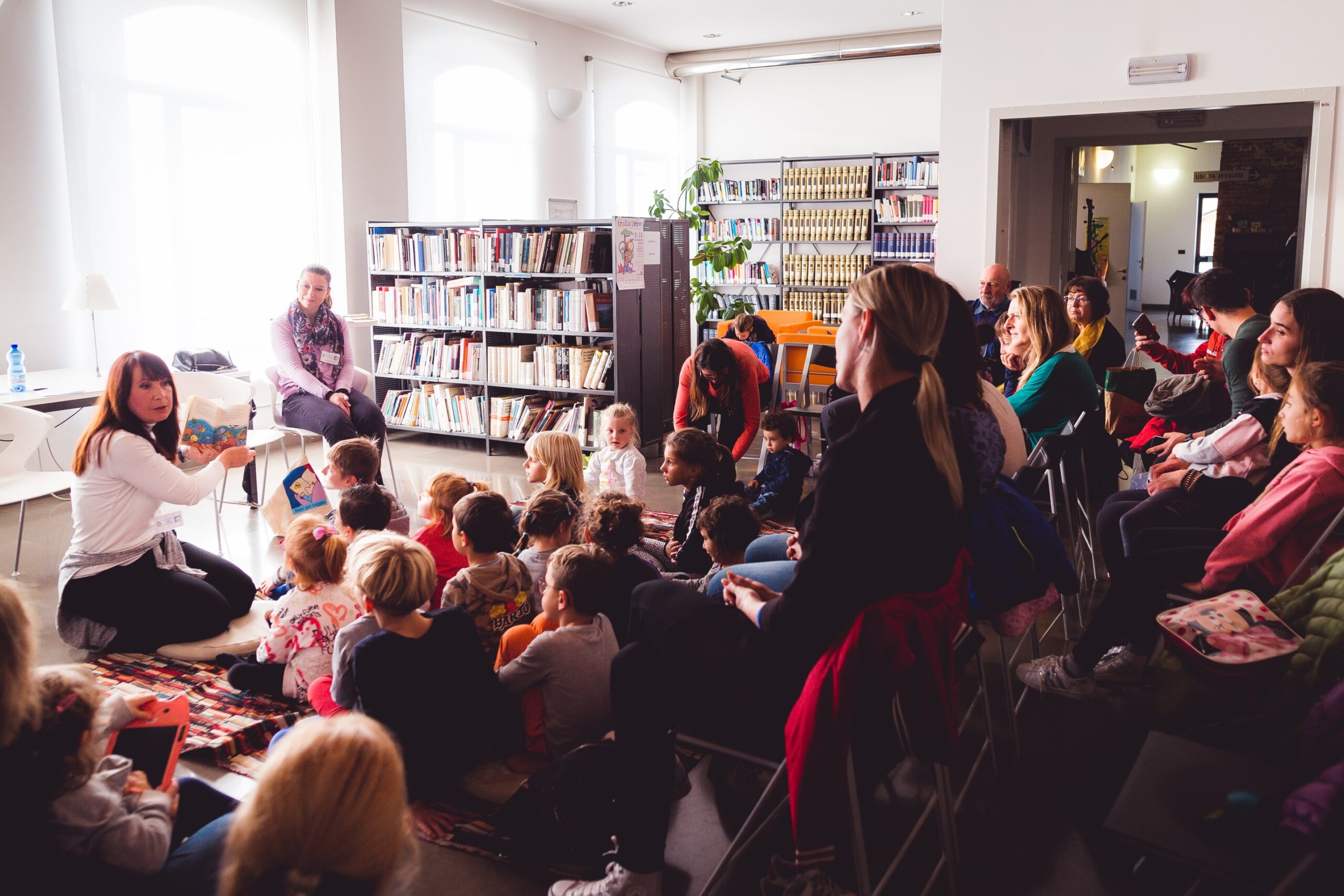 donna legge un libro ad alta voce ai bambini seduti in biblioteca