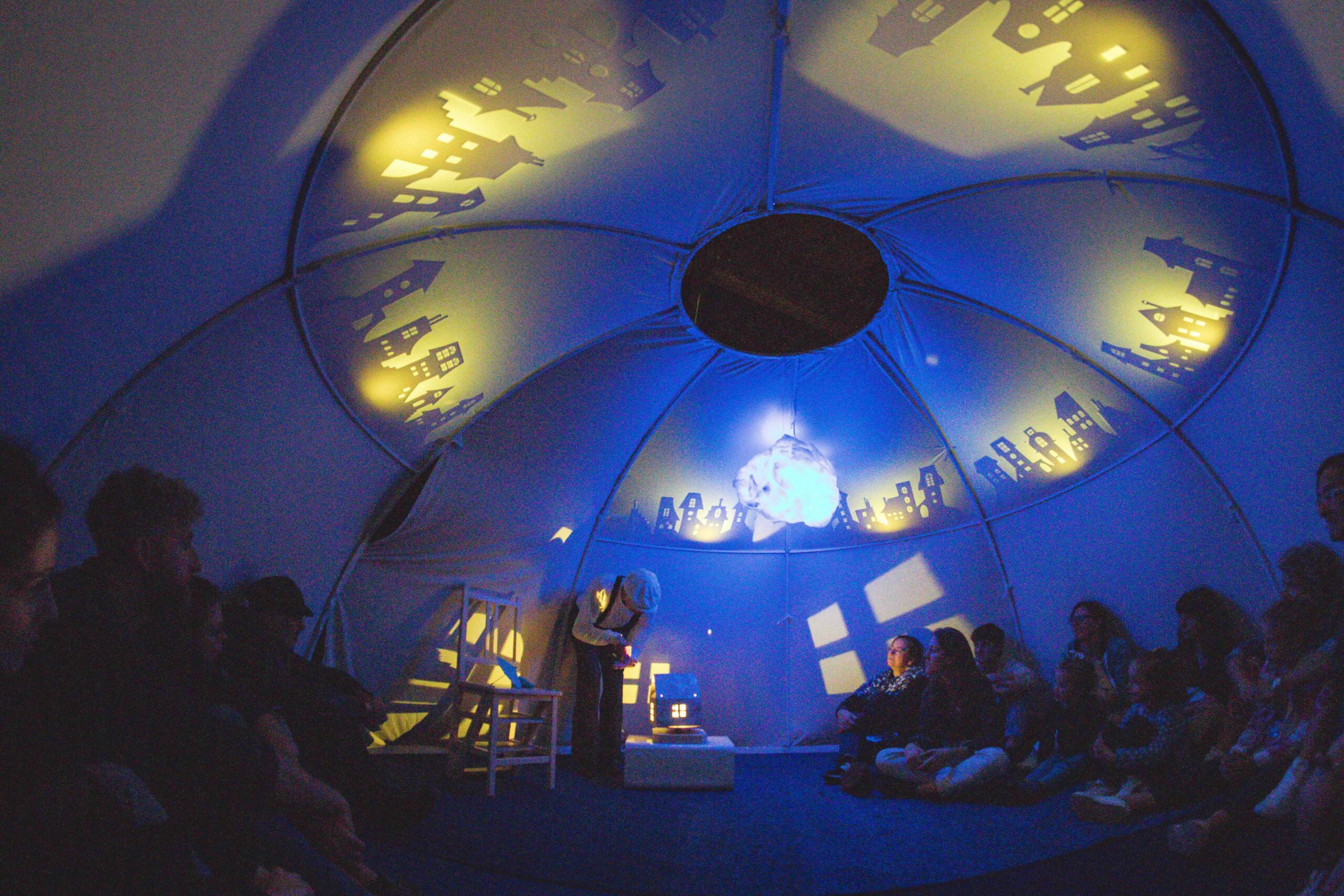 scena blu con immagini proiettate sulla tenda all'interno della quale l'attore recita rivolgendosi al pubblico di famiglie